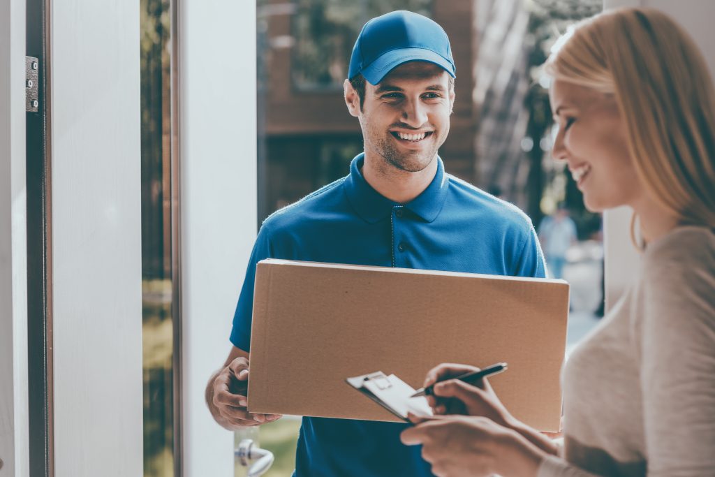 Smiling young delivery person holding a cardboard box while someone signs